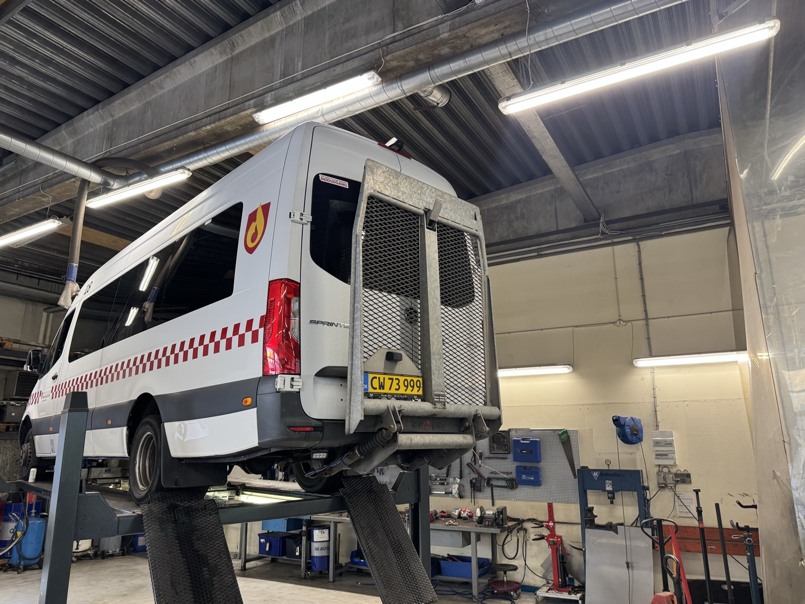Varevogn med bagsmæklift løftet på lift hos NP Autoteknik